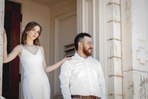 A couple stands in a doorway wearing coordinated white and beige outfits.