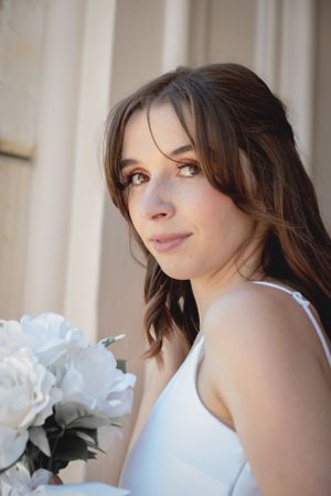 A close-up portrait of someone holding white flowers in a wedding dress.