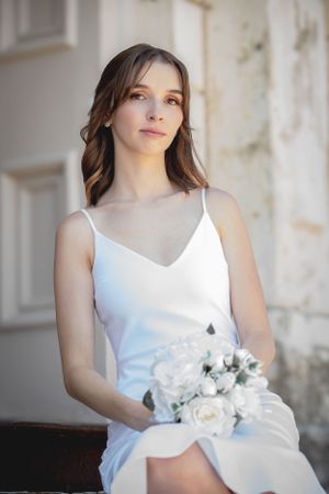 A person in a white dress sits holding a bouquet of white roses.