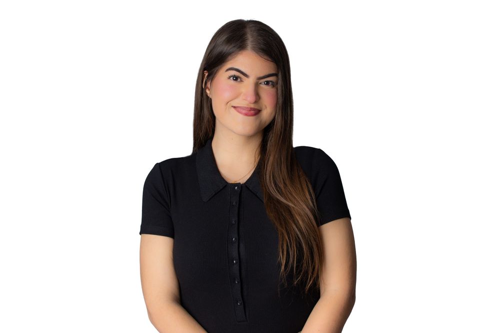 Studio portrait of a woman with long brown hair wearing a black collared shirt.