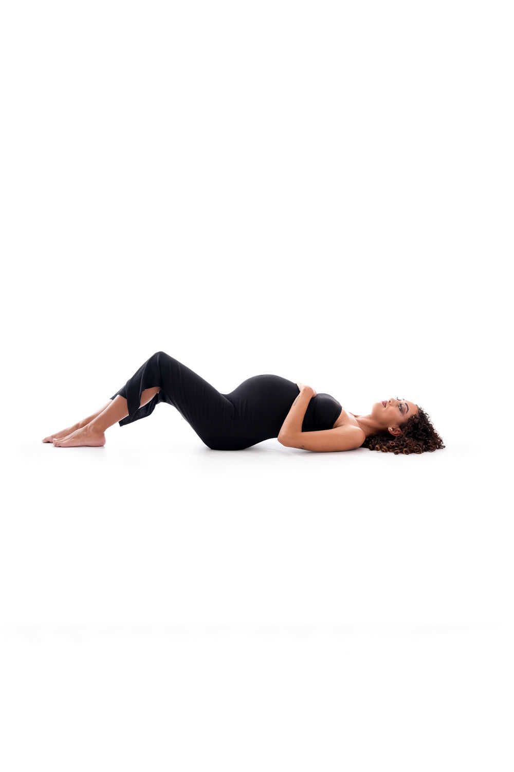 Personne en tenue d'entraînement noire allongée sur le dos, les genoux pliés dans une pose de relaxation ou d'exercice sur fond blanc.