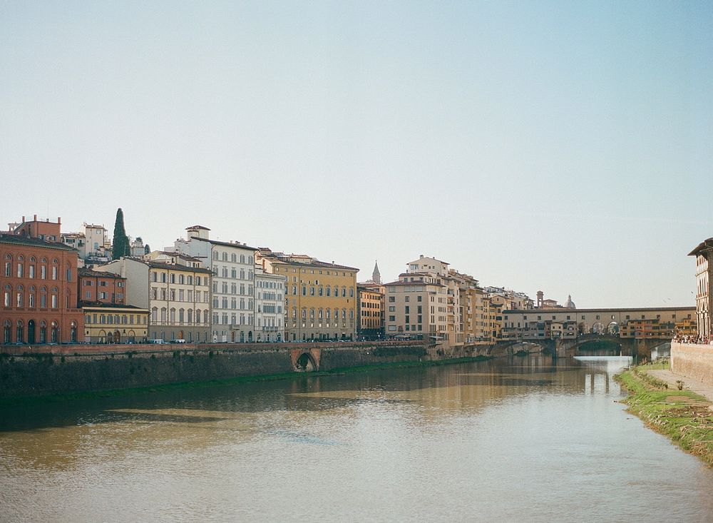 Historic buildings line the Arno River with Ponte Vecchio bridge visible in Florence, Italy.