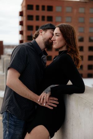Romantic couple shares an intimate moment on an urban rooftop with brick building in background.