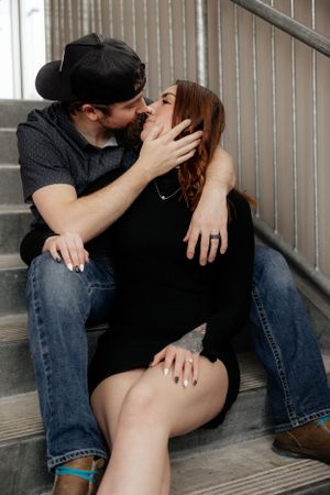 A couple in casual outfits sharing an intimate moment while sitting on concrete steps.