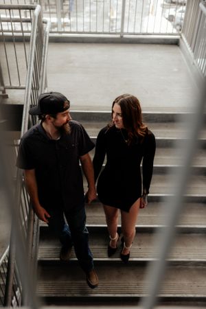 A couple dressed in black outfits share an intimate moment while walking down concrete stairs in an urban setting.