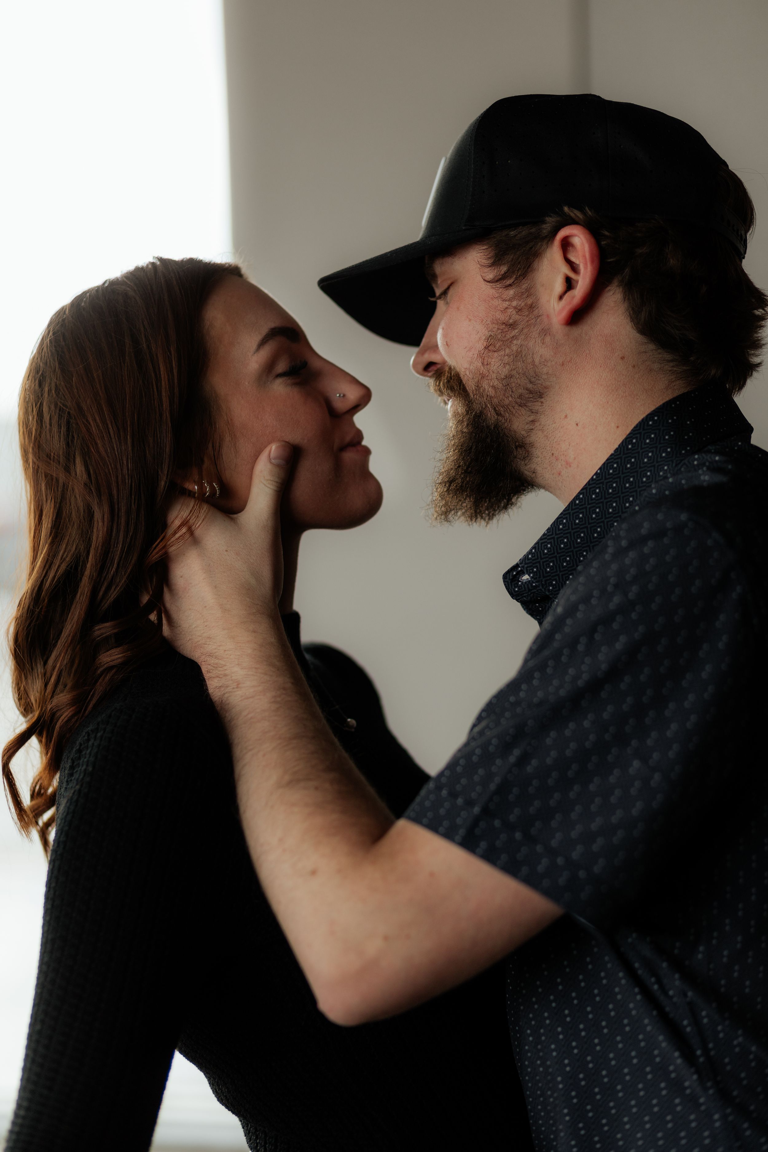 Intimate couple sharing a tender moment as they gaze at each other against a light background.