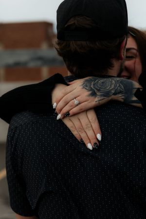 Close-up of hands embracing showing a rose tattoo and engagement ring.