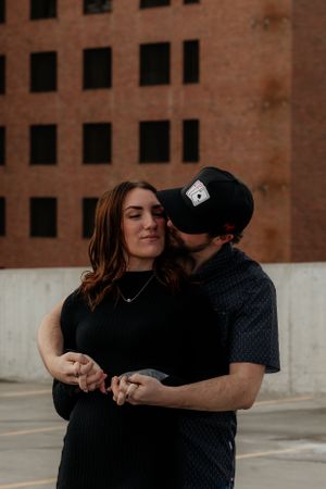 Intimate couple embraces in front of a brick building on a moody afternoon.