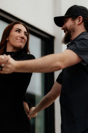 A couple holds hands and dances together in a tender moment captured against a dark background.