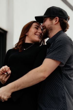 Couple sharing a tender moment while holding hands against a white wall.