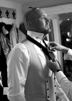 Black and white photo of groom having his tie adjusted while getting ready for his wedding.