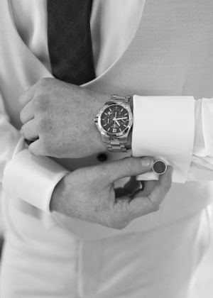 Close-up black and white photo of groom adjusting silver watch and cufflinks before wedding.