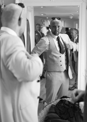 Black and white mirror reflection of groom in three-piece suit preparing for his wedding day.