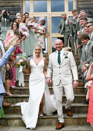 Bride and groom walk through confetti shower on venue steps surrounded by cheering wedding guests.