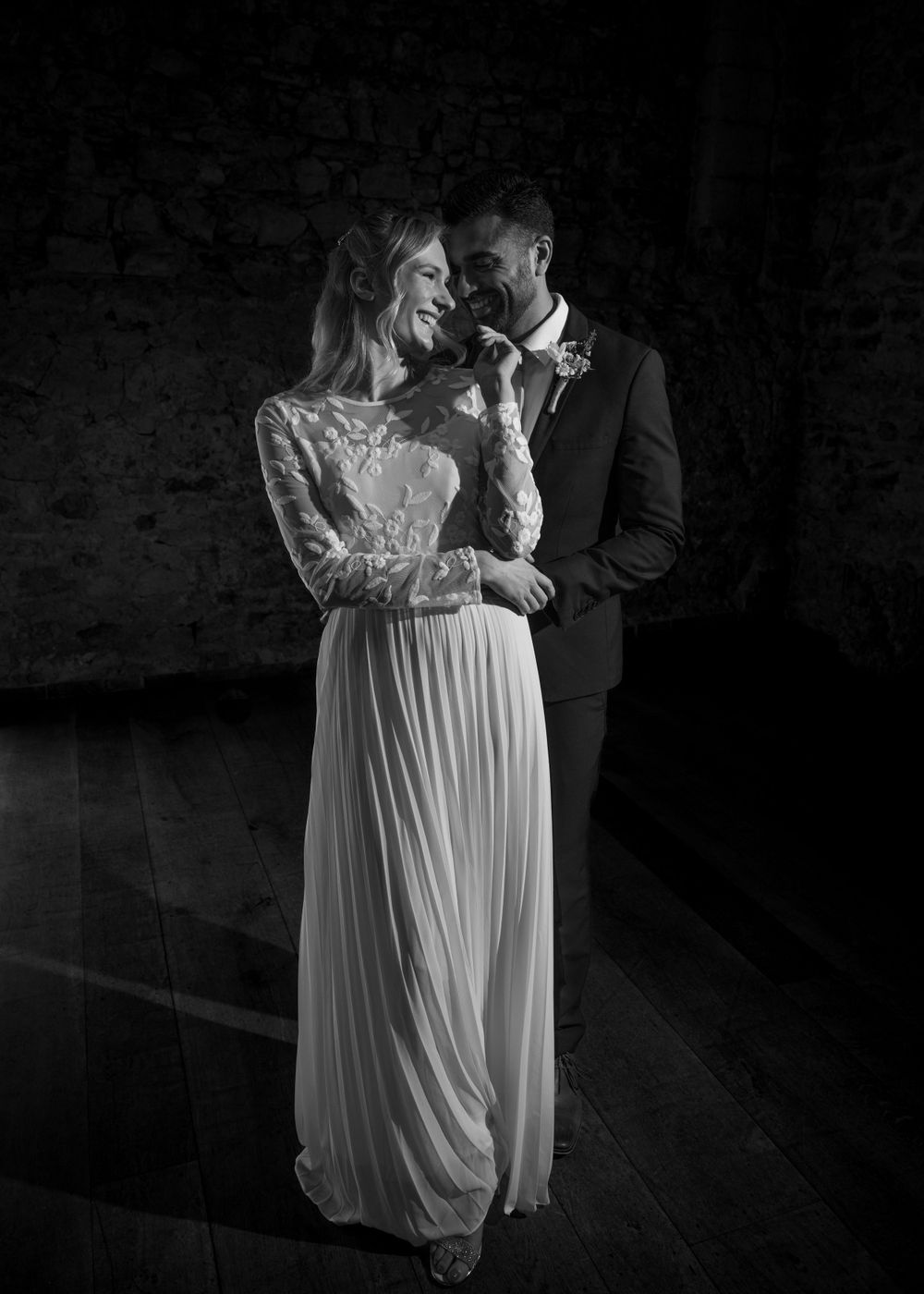 Elegant black and white wedding photo of smiling bride in lace gown and groom in dark suit sharing a tender moment.