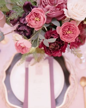 Lush pink and burgundy rose centerpiece on a gold-rimmed plate at a romantic wedding reception.