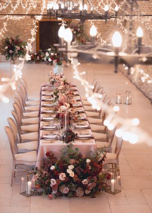 Stunning long wedding reception table adorned with lush floral arrangements and fairy lights in a barn.