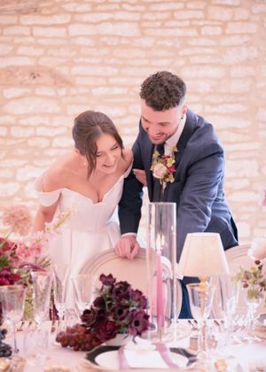 Joyful bride and groom in navy suit laughing together at elegantly decorated wedding reception table with floral centerpieces.