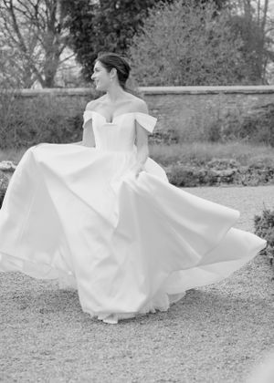 Bride twirling in an off-shoulder ballgown in a black and white outdoor wedding photo.