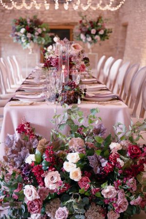 Elegant wedding reception table with pink linen and lush burgundy and blush floral centerpieces.