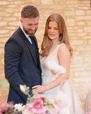 Smiling groom in navy suit with bride in lace wedding gown sharing a tender moment outdoors.