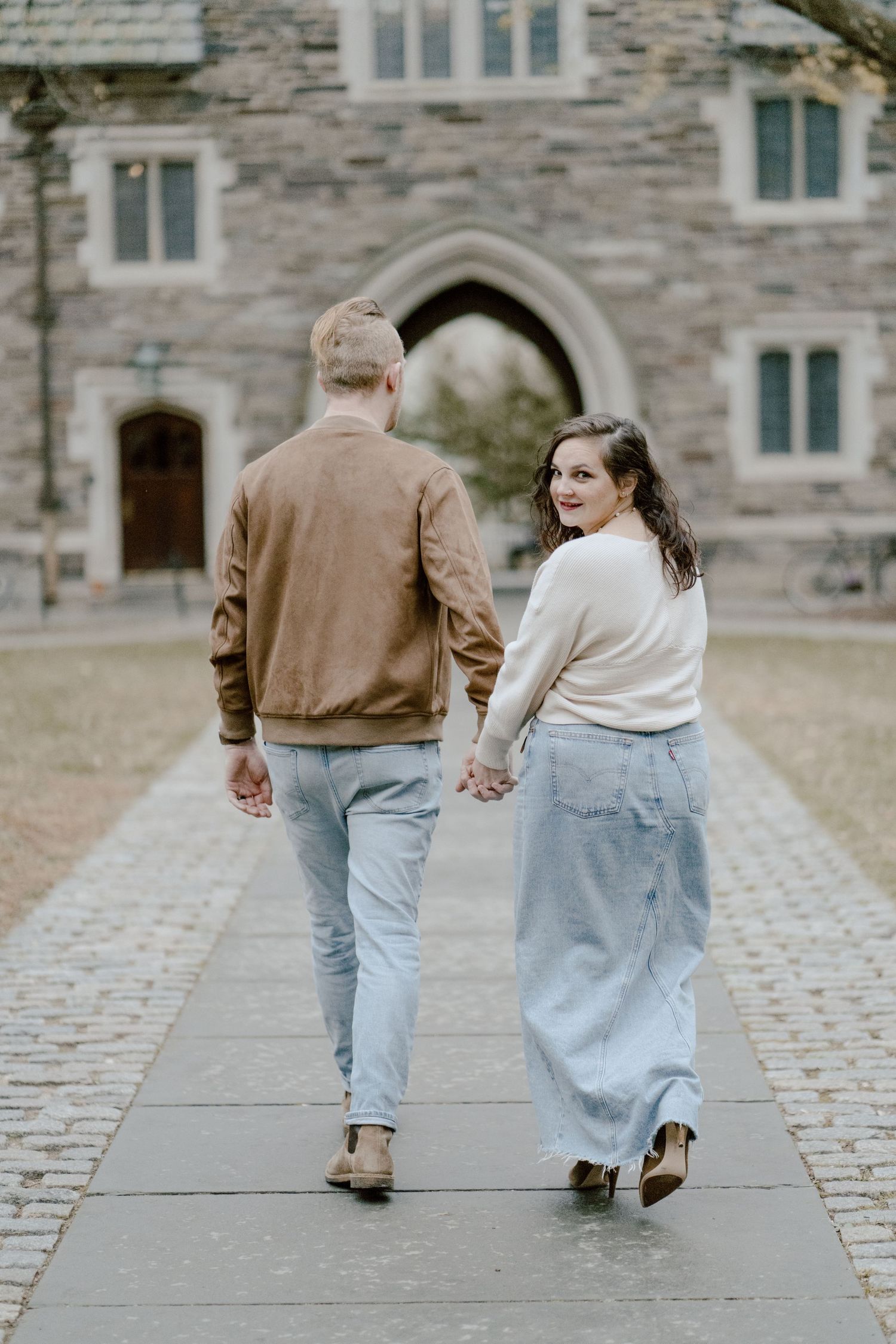 Couple walking away hand in hand on stone path near historic building.