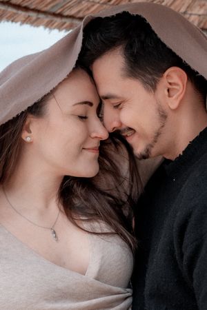 Romantic close-up portrait of couple with tender expressions under soft beige wrap.