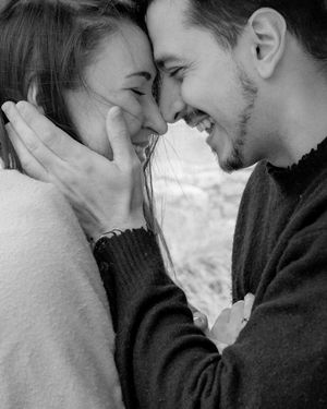A romantic black and white photo of a couple sharing an intimate moment while smiling and touching foreheads.