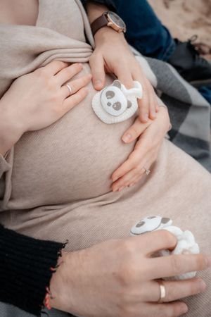 Close-up of hands holding panda-themed baby items against a cozy sweater.