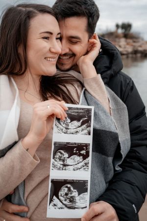 Happy couple sharing ultrasound photos of their baby during a pregnancy announcement photoshoot by the water.