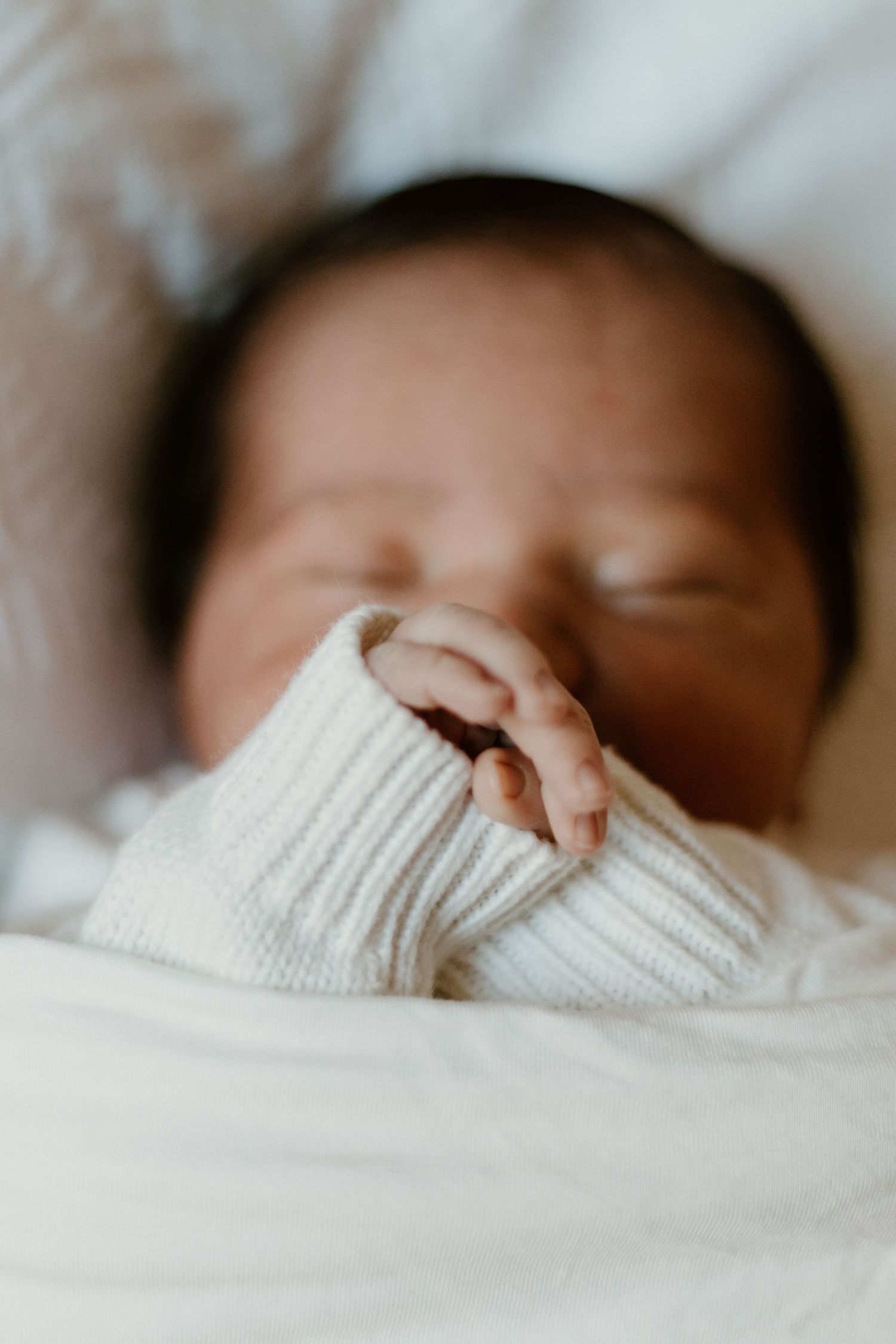 Close up of a newborn baby laying on a bed, wrapped in a blanket with his hands on his face