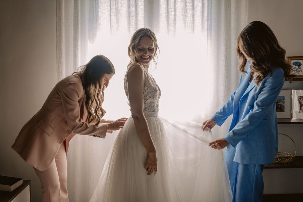 Giovane sposa indossa l'abito nuziale mentre due amiche le sistemo il velo