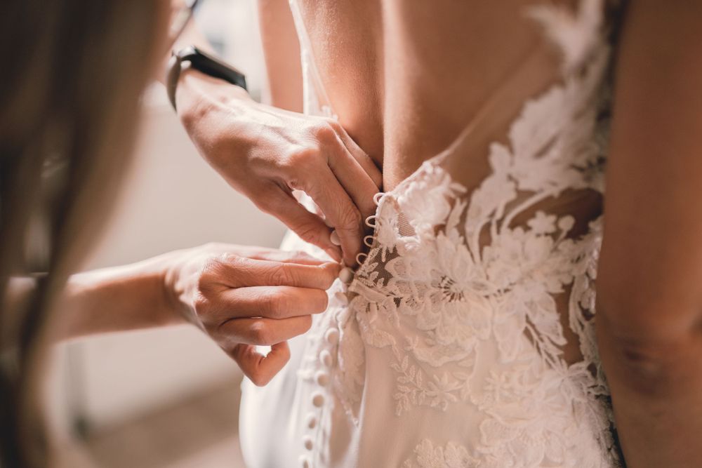 Dettaglio di una damigella che allaccia i bottoni dell'abito della sposa sulla schiena