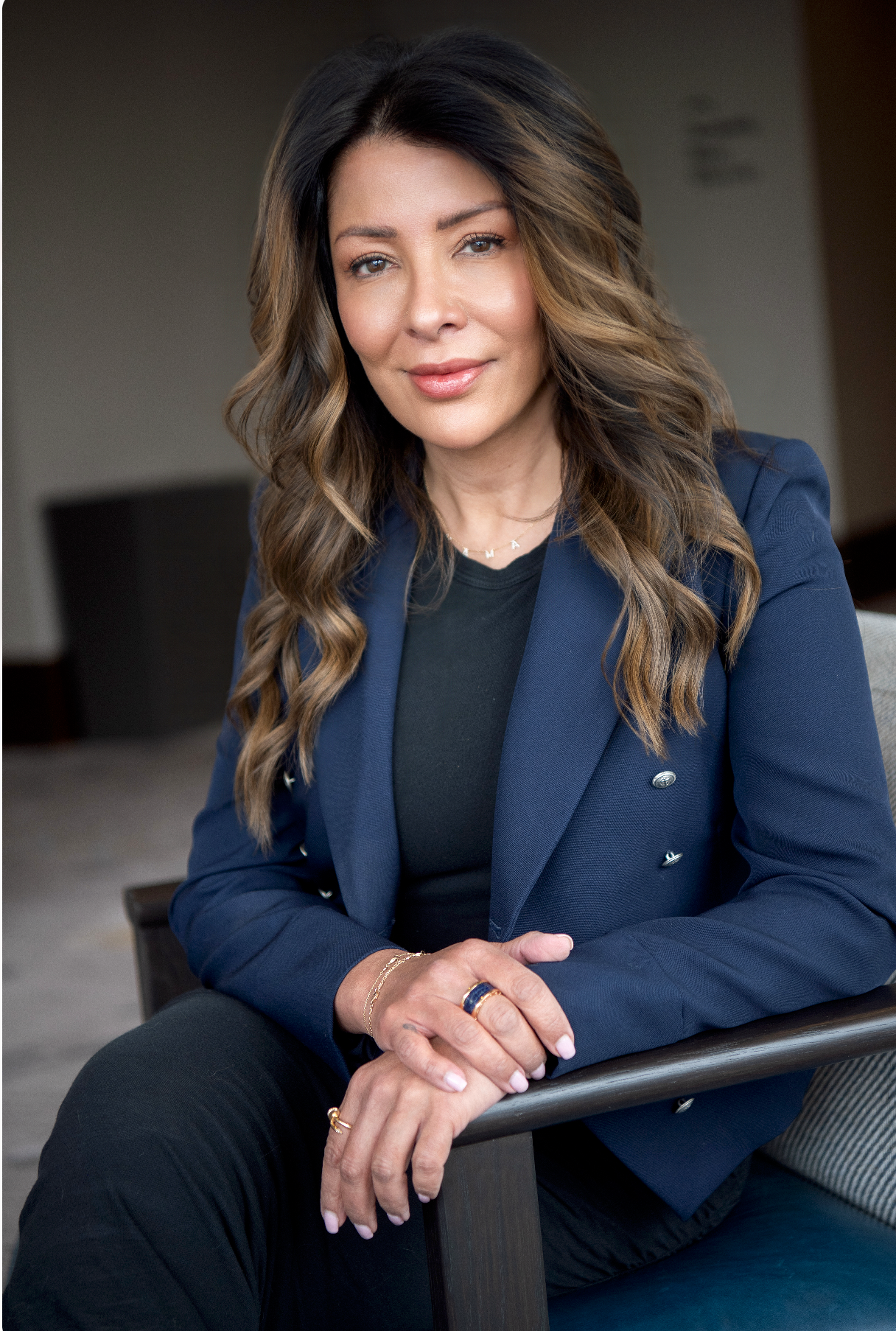 Professional woman in navy blazer with long wavy hair poses confidently in a modern office setting.