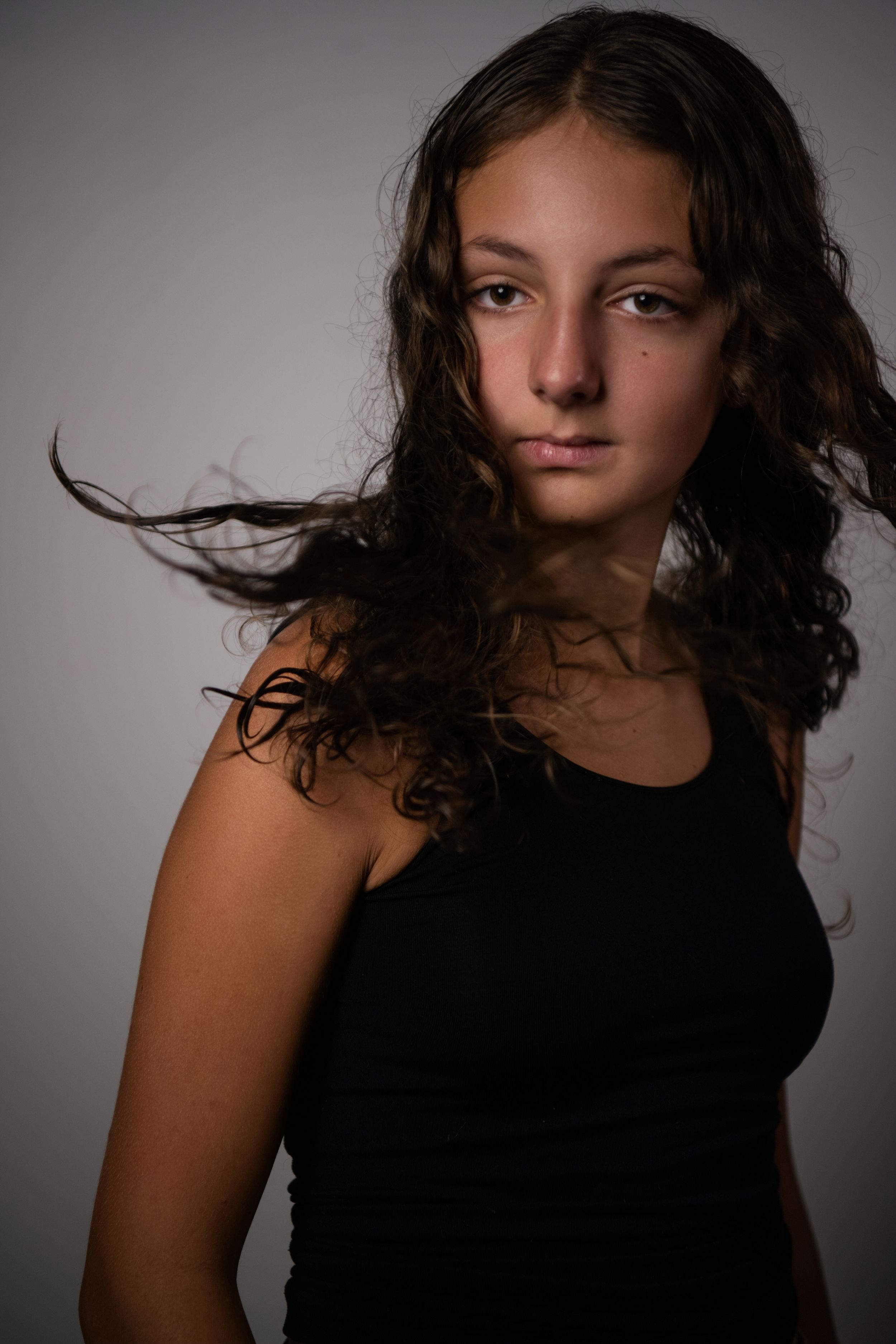 Portrait series showing dynamic movement of dark curly hair against a gray background in dramatic lighting.