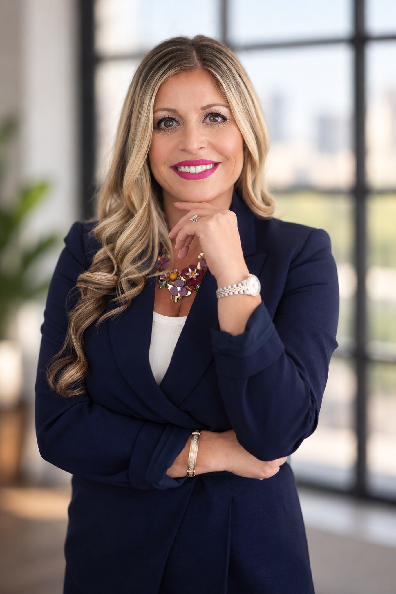 Professional woman in navy blazer with blonde hair smiling confidently in a modern office setting.
