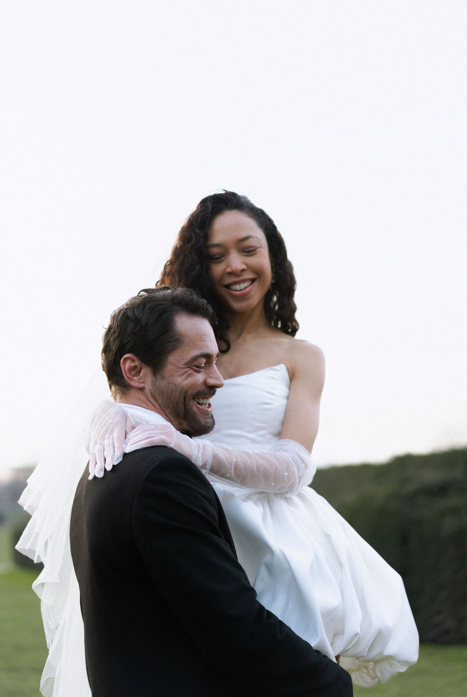 A joyful wedding couple embraces outdoors with the groom holding his bride in a romantic candid moment.