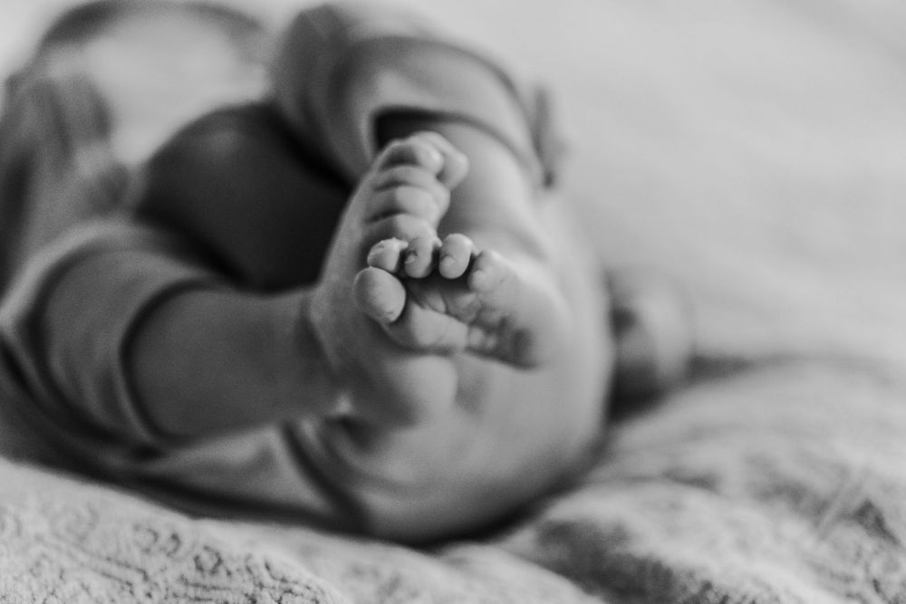 Black and white close-up photo of a newborn baby's tiny feet and toes resting on a soft blanket.