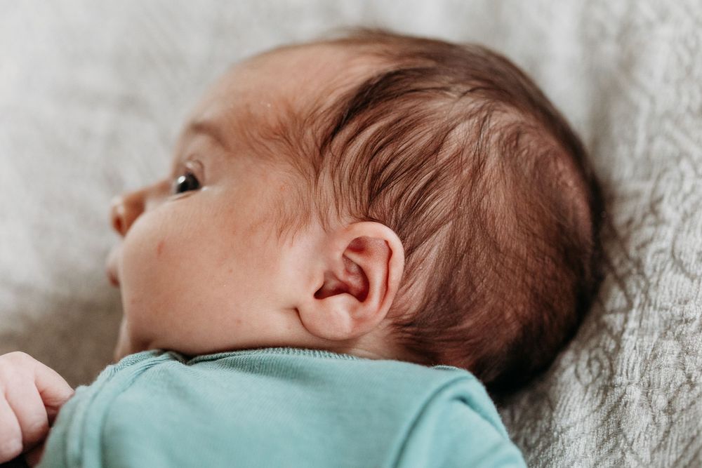 Close-up profile of sleeping newborn baby wearing teal onesie on gray blanket.