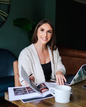 Person working at wooden table with laptop and papers in modern interior setting.