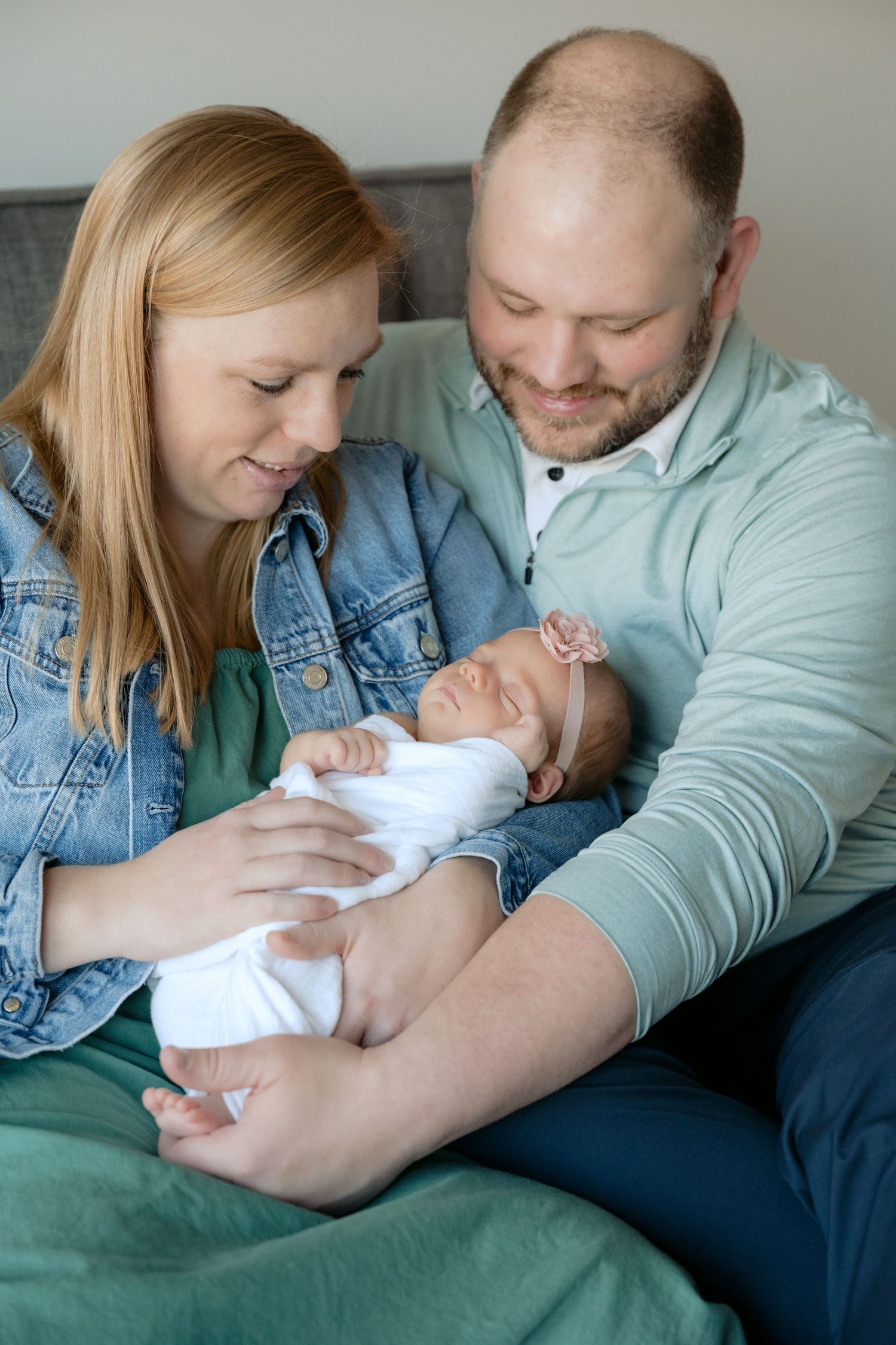 parents gaze lovingly at sleeping, swaddled newborn while snuggling on their bed during in home lifestyle newborn session in lake elmo, mn