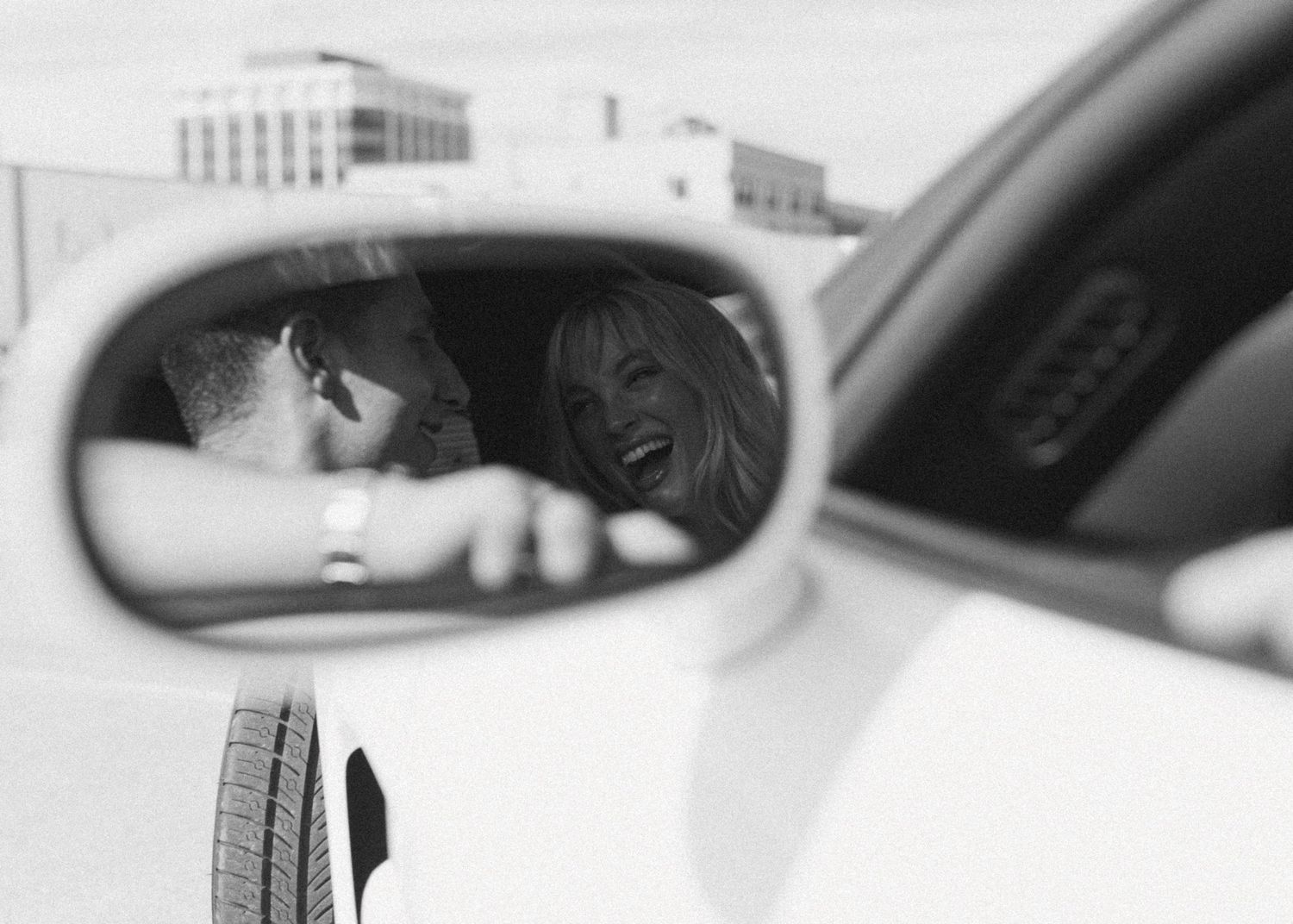 Parents kneeling on grass encouraging their toddler daughter to walk toward them in black and white.