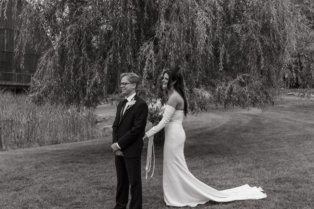 Black and white wedding photo of bride and groom standing together under a weeping willow tree.