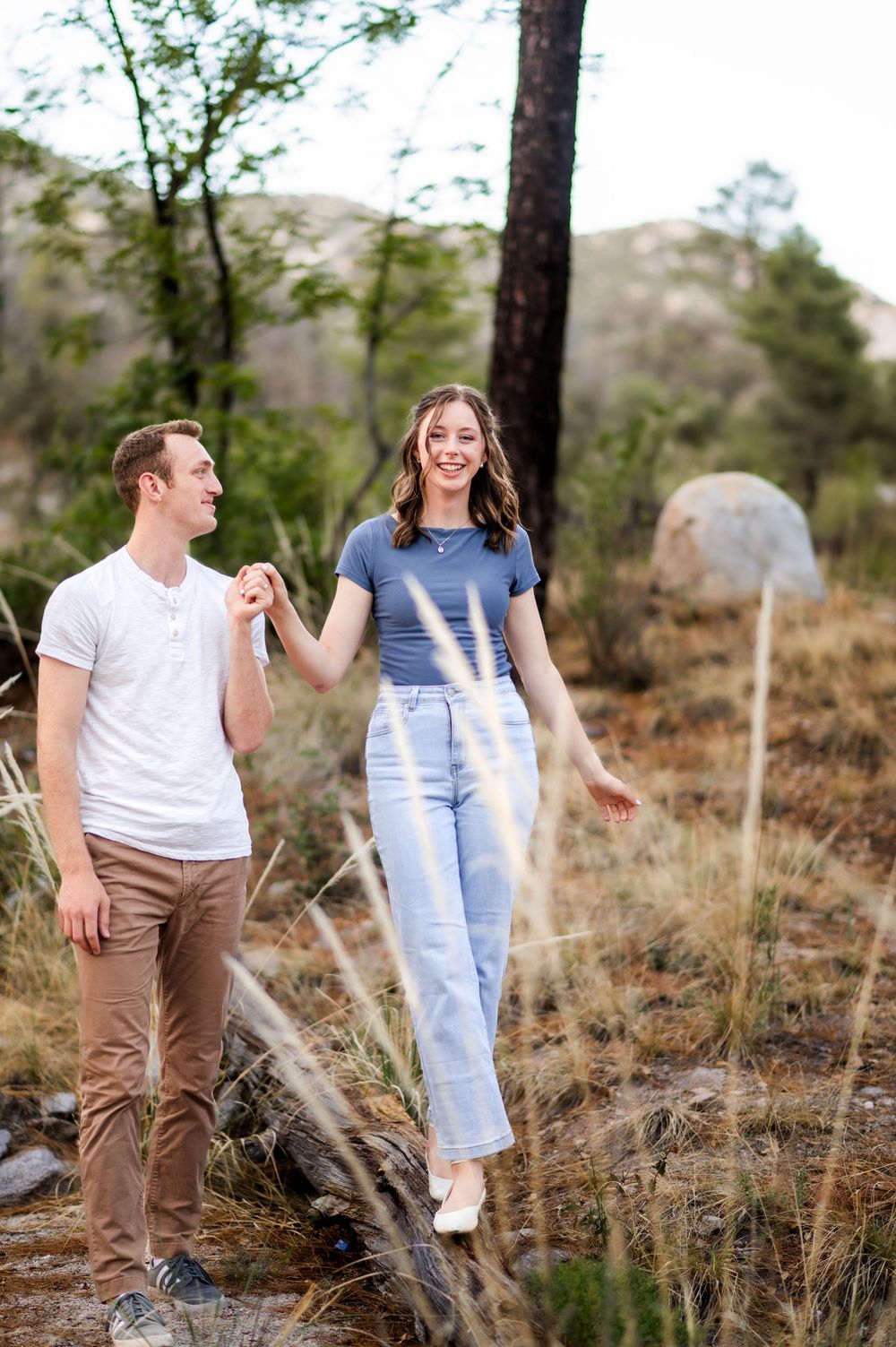 Happy couple walks hand in hand through a rocky mountain forest trail together.