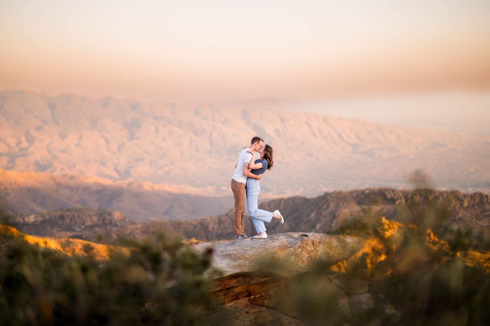 Couple embraces on a rocky mountain summit with stunning panoramic valley views.