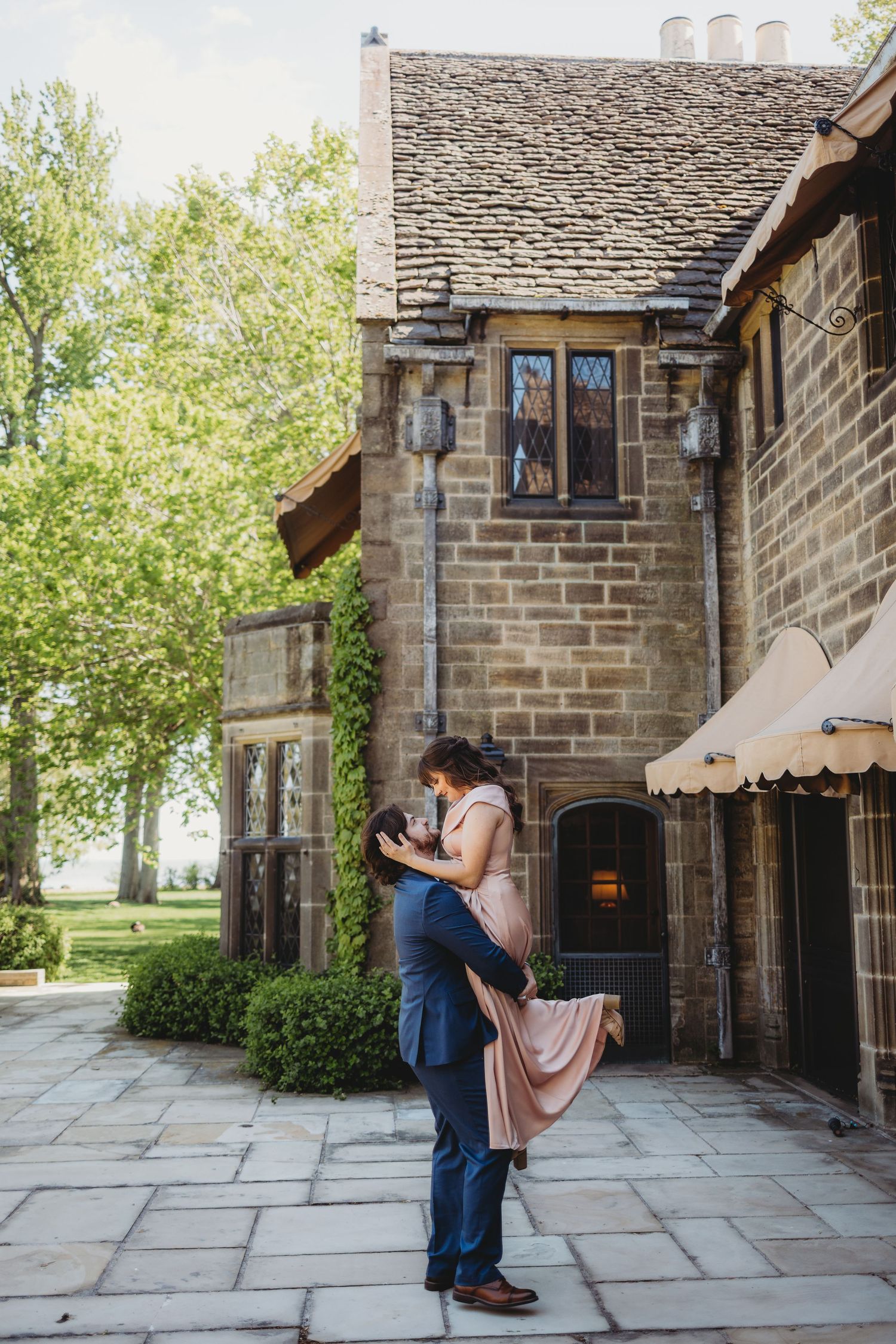 Couple sharing a romantic embrace outside a charming stone building during an outdoor engagement photo session.