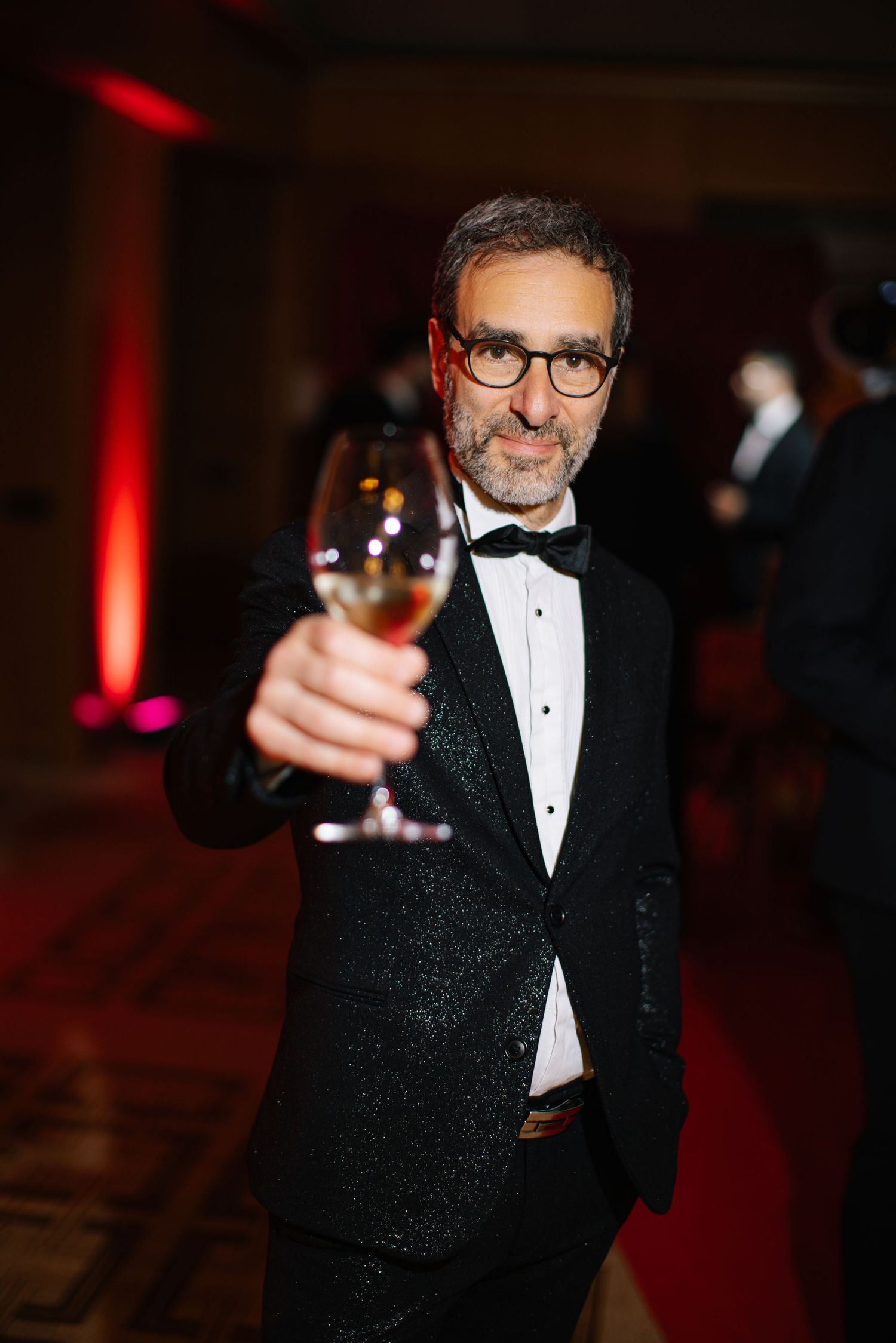 Elegant man in black tuxedo and bow tie toasting with champagne glass at formal gala event.