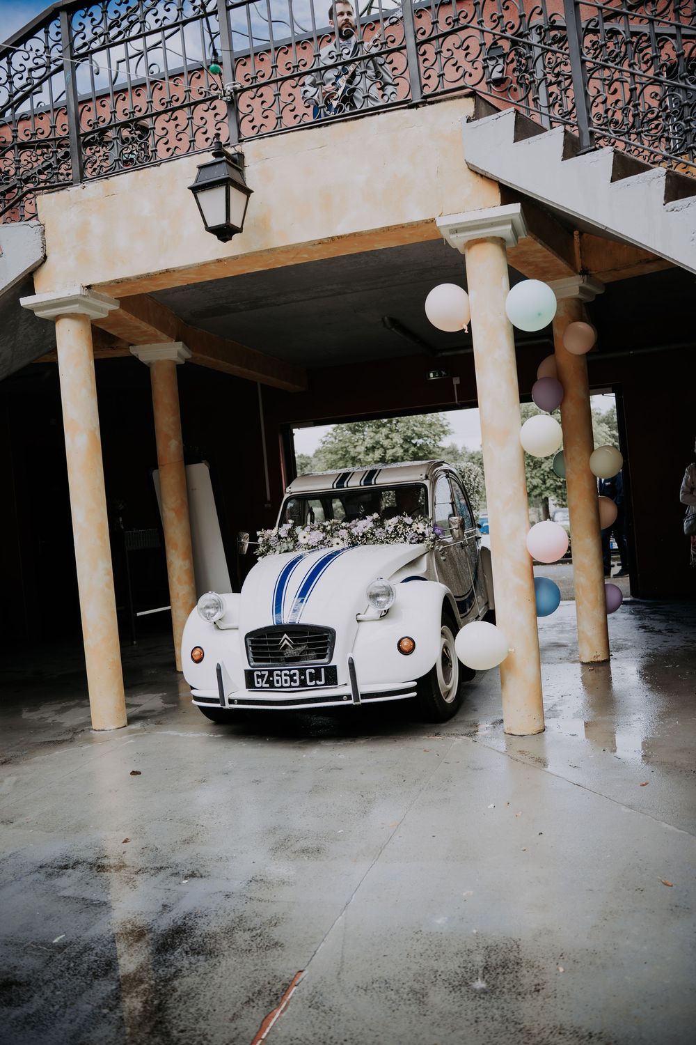 Vintage white Citroen 2CV wedding car decorated with balloons parked under ornate building entrance.