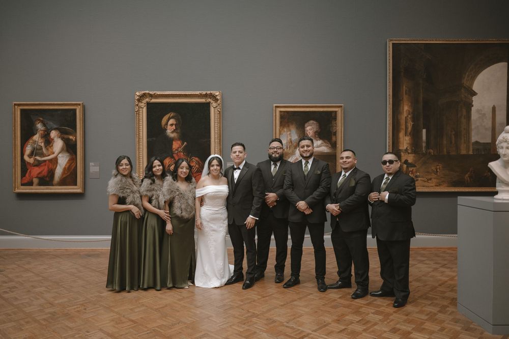 Wedding party poses in art museum gallery, bridesmaids in olive gowns and groomsmen in dark suits.