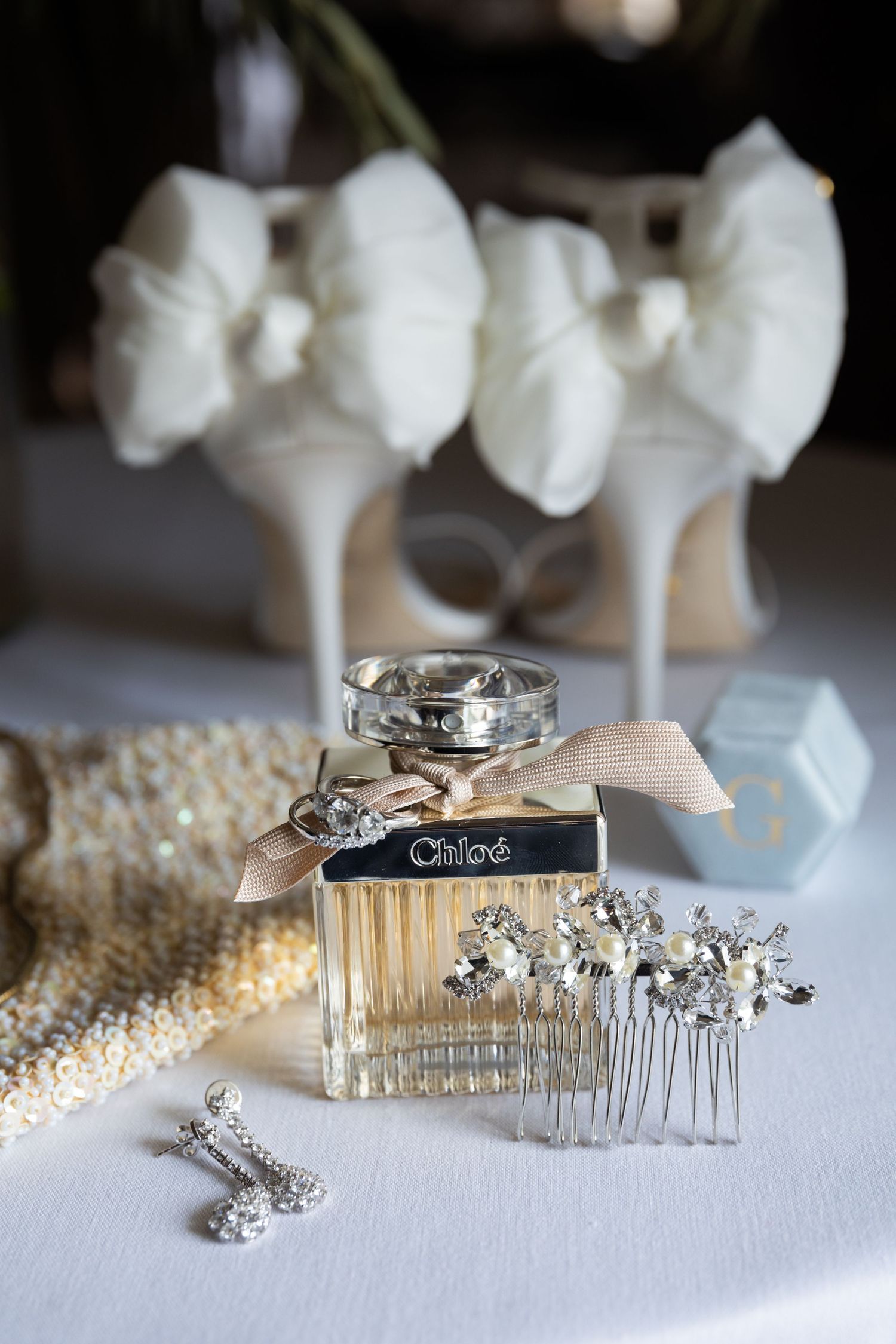 Chloé perfume bottle with crystal hair comb, diamond earrings, pearl accessories, and white heels in soft bridal flat lay.